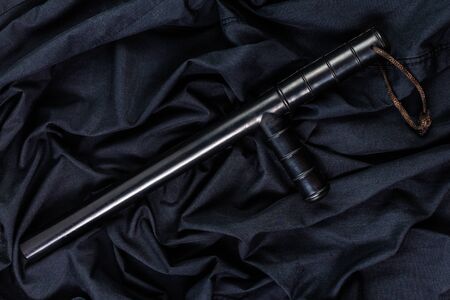 black rubber police baton on black shirt wrinkled cloth low-key flat layの写真素材