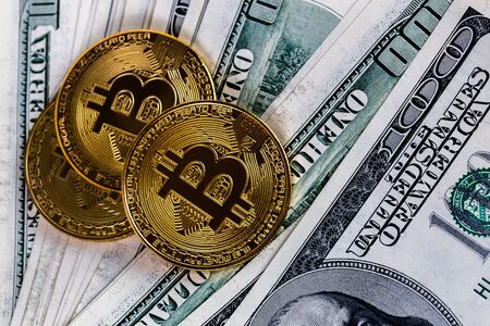 three bitcoin shiners over paper us dollar banknotes background close-up with selective focus and blurの写真素材