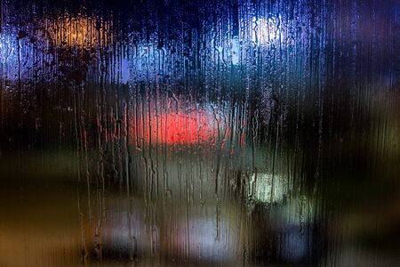 an abstract background night street lights bokeh through wet glass, close-up with selective focusの写真素材