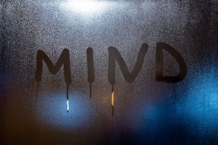 the word mind written on night wet window glass close-up with blurred backgroundの写真素材