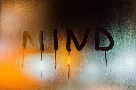 the word mind written on night wet window glass close-up with blurred orange backgroundの写真素材