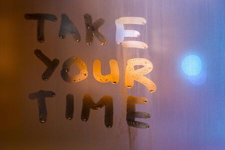 the phrase take your time written by finger on night wet glass with blurred street lights, close-up with selective focusの写真素材