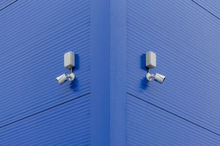 two small white security cameras on blue steel building corner.