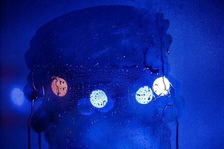 an abstract background of blue tone night street lights bokeh trough half-wiped wet glass with...