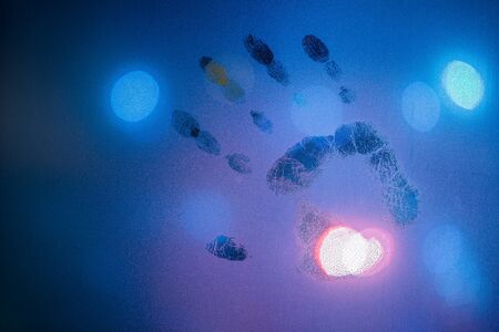 handprint on night wet glass in cold blue colors with blurry street light in backroundの写真素材