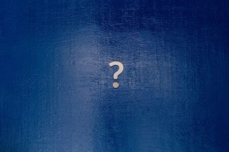 A small white metal question sign on center of dark blue painted board - flat lay coneptの写真素材