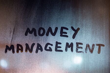 the words money management handwritten on night wet window glass with selective focus and blur in backgroundの写真素材