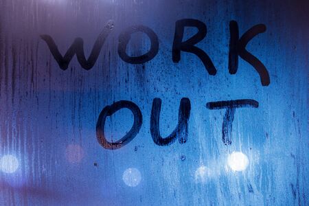 The words work out written on night sweaty window glass with blurred blue light in the background