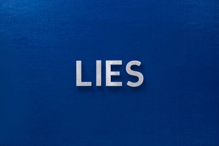 the word lie laid with silver metal letters on classic blue board in flat lay with central composition.の写真素材