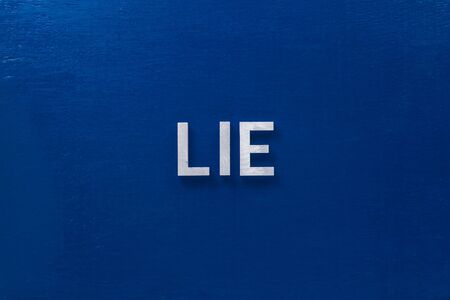 the word lies laid with silver metal letters on classic blue board in flat lay with central composition.の写真素材
