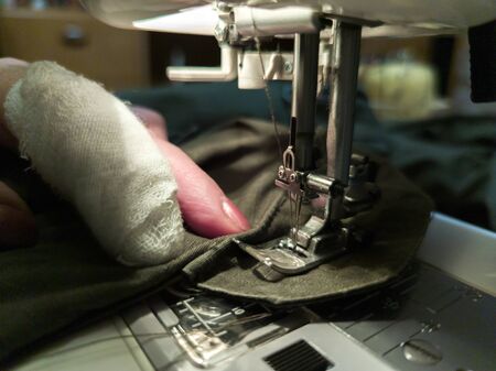 a hand of aged womans with a bandaged finger sews with a sewing machine