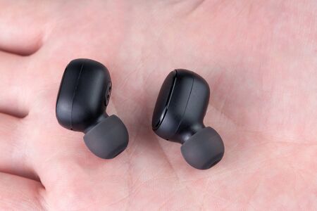 a pair of black wireless earbuds laying on caucasian palm - close-up with selective focus