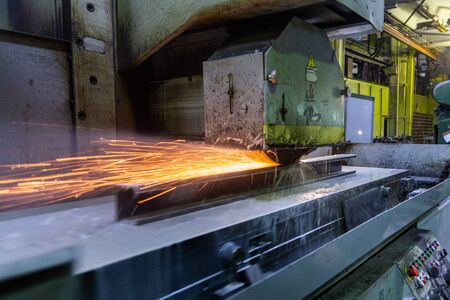 a process of flat surface grinding with a lot of sparks and liquid cooling indoors at metalworking shop, old factory equipment at workの写真素材