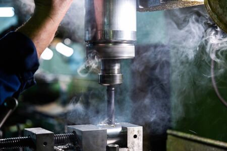 Industrial steel drilling with smoke close-up with selective focus. Manual feed by hand. Workpiece...