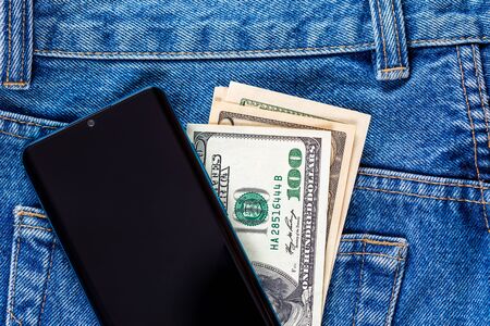 US dollar banknotes and smartphone over the left rear pocket of blue jeans. Concept of saving money or pocket expenses.の写真素材