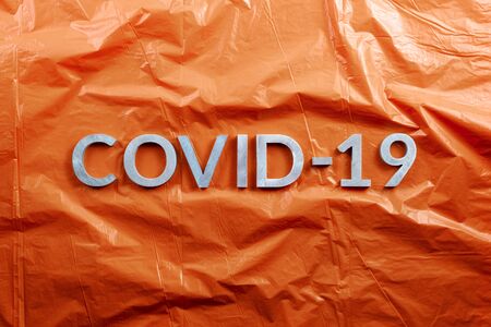 The word COVID-19 laid with aluminium letters on crumpled orange plastic film background in flat lay composition, directly above view.の写真素材