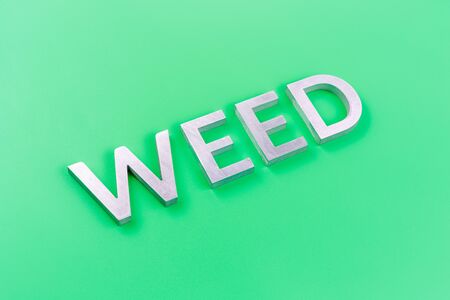 the word weed laid with silver metal letters on pastel green background with diagonal perspective and selective focusの写真素材