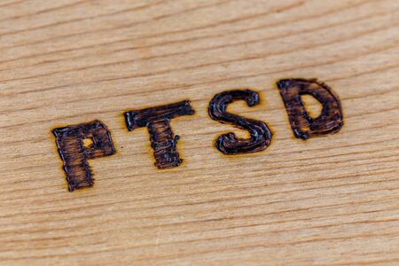 an abbreviation PTSD - post traumatic stress disorder - burned by hand on flat wooden board in diagonal compositionの写真素材
