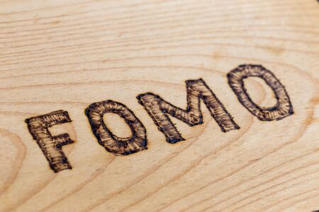 Abbreviation FOMO - fear of missing out - burnt by hand on flat wooden surface. Diagonal close-up view with selective focus.の写真素材