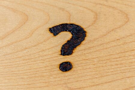 question mark drawn with handheld woodburner on bright flat wooden surface with selective focus and...