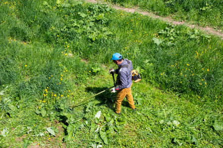TULA, RUSSIA - MAY 19, 2020: Russian official lawnmower worker man cutting green grass with two-cycle engine string trimmer. Top to down view with selective focus.のeditorial素材