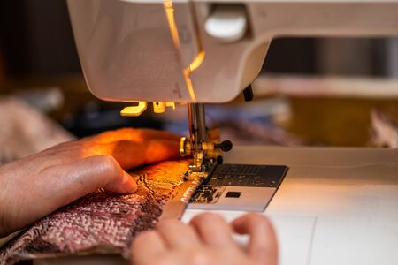 a close-up view of sewing process, hand of old woman using sewing machine, selective focus technique