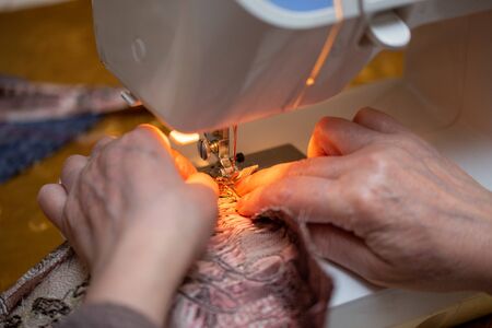 a close-up view of sewing process, hand of old woman using sewing machine, selective focus technique