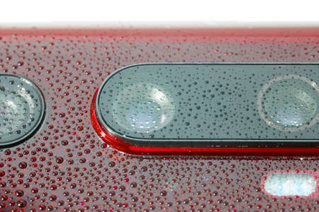 red phone camera lens covered with small water drops - close-up with selective focus and blur