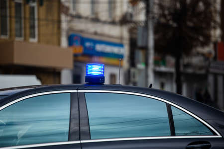 blue flashing light on top of black government car on daytime city street