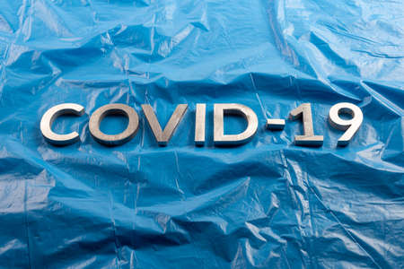 The word COVID-19 laid with aluminium letters on crumpled blue plastic film background in flat lay compositionの写真素材