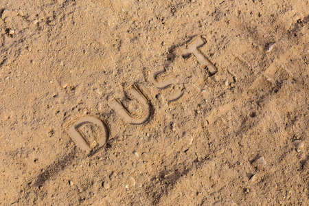 the word dust physically imprinted on dusty road surface in flat lay perspective