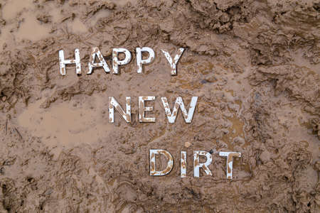 the words happy new dirt laid with silver metal letters on wet mud surfaceの写真素材