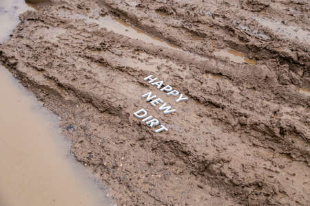 the words happy new dirt laid with silver metal letters on wet mud surface