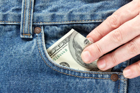 hand takes US dollar banknote from the right front pocket of blue jeans. Concept of saving money or...