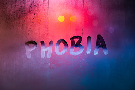 the word phobia handwritten on wet foggy window glass surface with red-blue background lightsの写真素材