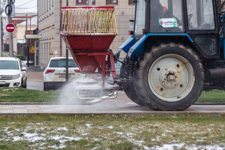 TULA, RUSSIA - NOVEMBER 21, 2020: Tractor spreading salt reagent on city pavement at winter daylight.のeditorial素材