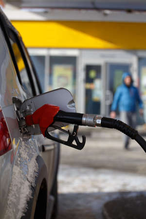 silver metallic color car refueling on winter day gas station - close-up with selective focus and...