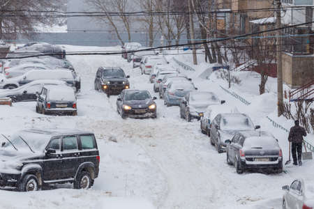 Two cars drive through a snowy yard between rows of parked cars in deep snow in Tula, Russia.のeditorial素材