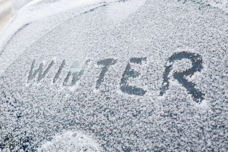 word winter handwritten on snowy car window at winter morning light