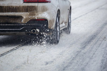 Road snow pieces flow from wheels of dirty white car moving fast in daylight city with selective...