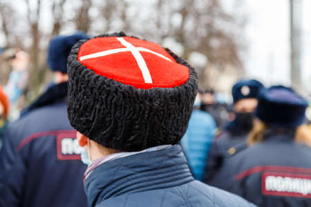 man in cossack hat with white cross on red watching blurry crowd of peopleの写真素材
