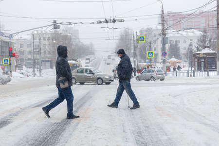 Tula, Russia - February 13, 2020: Two men crossing city road during heavy snow fall.のeditorial素材