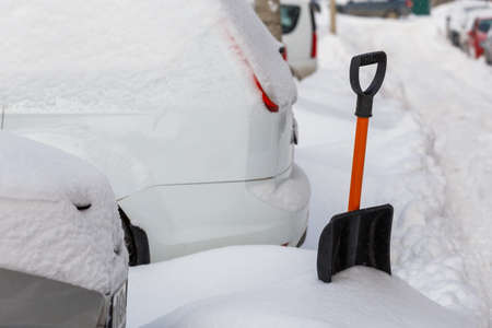 small plastic snow shovel near snow-covered cars at sunny winter morning
