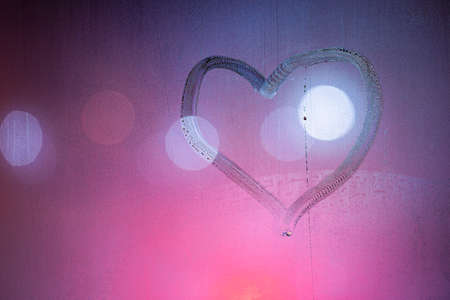 heart symbol hand drawn on wet night window glass in pink colorsの写真素材
