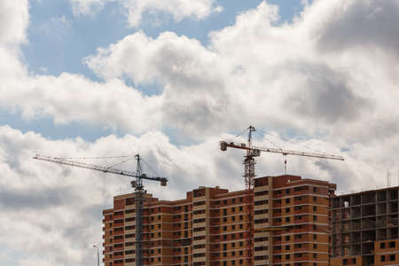 building process of large residential apartment building with crane on cloudy sky background
