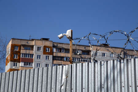 residential multi-storey building behind a fence with barbed wire and small surveillance camera