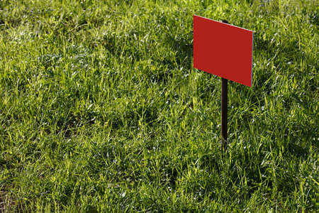 blank red sign mockup on green lawn background - close-up with selective focusの写真素材