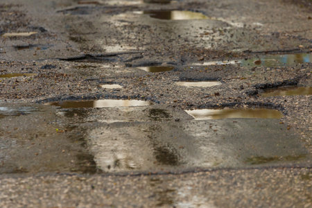 potholes and puddles on bad broken wet asphalt road after rainの写真素材