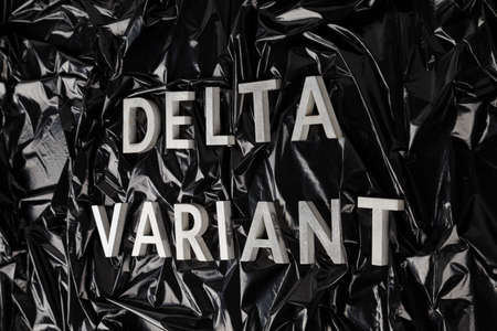 words delta variant laid with silver metal letters on crumpled black plastic bag background in...