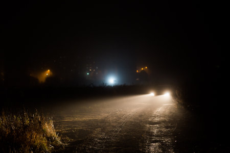 car headlight cones in night fog at field behind cityの写真素材